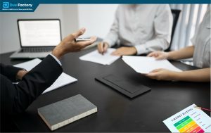 A man holds a laptop while a woman sits at a desk, engaged in a discussion about credit counselling.